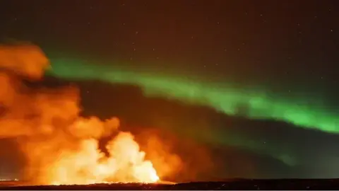 Volcano spews ash and smoke against the backdrop of the Northern Lights.