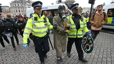 PA Media A protester wearing a gasmask and boiler suit with police