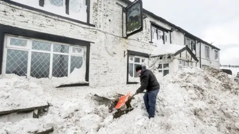 PA Landlord Angus Wharton clears snow outside the Ye Olde Black Ladd pub in Shaw, Greater Manchester.