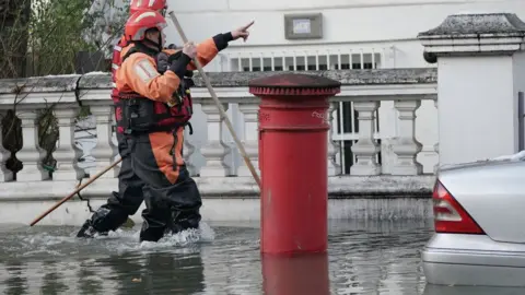 PA Media Fire crews wading through flood water