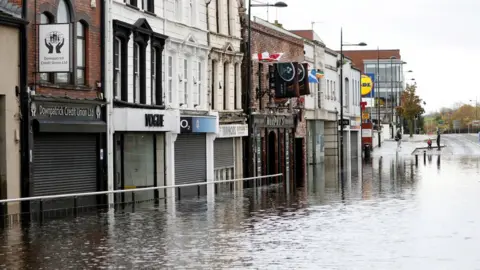 PA Media Deep floodwater outside business premises on Downpatrick's main shopping street