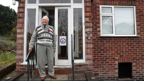 PA Media World War Two veteran John Maffey 93, stands on his doorstep in Knutsford, Cheshire, during the two minutes silence