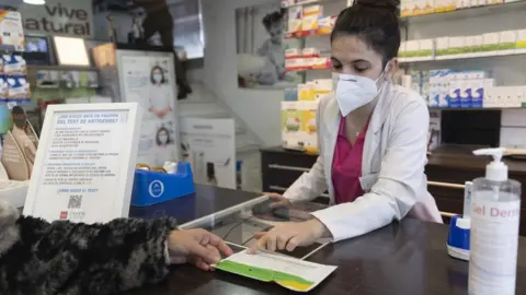 Europa Press News/Getty Images A pharmacist shows an antigen test to a person at 'Las Gemelas' pharmacy, on 10 January, 2022 in Madrid, Spain