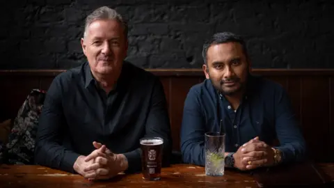 Piers Morgan and Amol Rajan sit at table with drinks