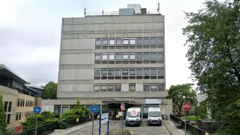 A grey building with five floors. Two ambulances are parked outside.