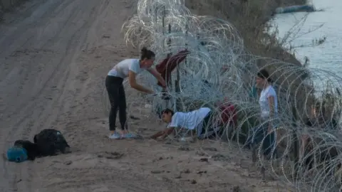 Reuters A migrant family attempts to navigate through concertina wire in Eagle Pass on 27 July