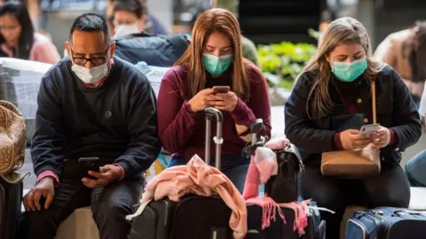 MARK RALSTON/Getty Images Passengers wear face masks to protect against the spread of the Coronavirus as they arrive on a flight from Asia at Los Angeles Airport