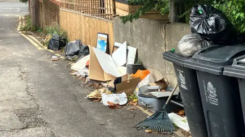 Rubbish on the street, it has cardboard, a broken frames and black bin bags