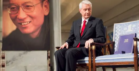 AFP Nobel Committee Chairman Thorbjorn Jagland sitting during the Peace Prize Ceremony in Oslo in front of a photo of Nobel peace laureate Liu Xiaobo