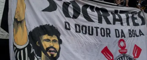 AFP Supporters of Corinthians stand next to a banner in homage of the late footballer Socrates, during the Brazilian Championship final date match against Palmeiras, at the Pacaembu stadium on 4 December 2011 in Sao Paulo, Brazil