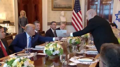 Benjamin Netanyahu hands a piece of paper to Donald Trump