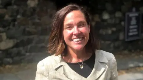 Melissa McCullough - a woman in a pale-coloured blazer and black top - smiling at the camera. She has shoulder-length brown hair.