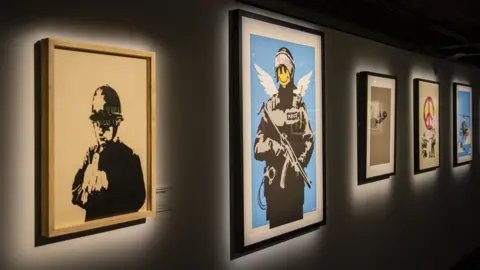 A series of Banksy works in frames on a wall