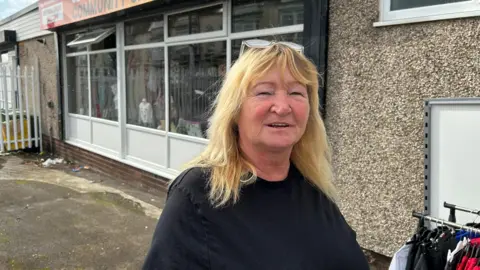 BBC Wendy English the founder of Second Chance Sunderland stands in front of their new store in Hendon. She had shoulder-length blonde hair and smiles at the camera.