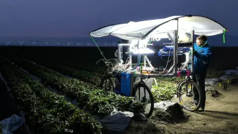 Mineral A man works on a prototype buggy in a field at night - this version looking like a large table mounted on bicycle wheels, with computer kit on the flat surface