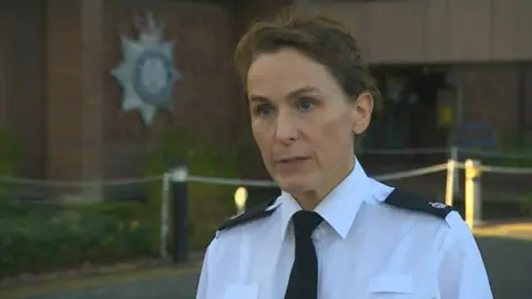 Det Ch Supt Jane Topping during an interview. She is standing outside Suffolk Police headquarters. She has short brown hair and wears a white shirt with a black tie and black lapels on the shoulders.