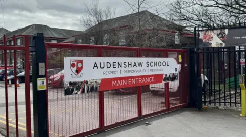 The red school gates at Audenshaw with the school building behind.
