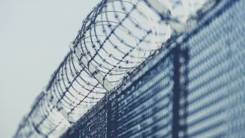 Getty Images Barbed wire on a prison wall