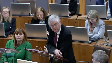 First Minister Mark Drakeford standing in the Senedd