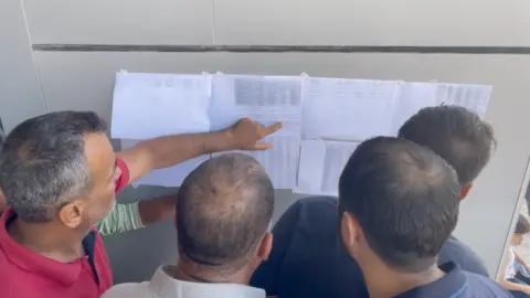 Men check lists of those allowed to leave Gaza at the Rafah crossing