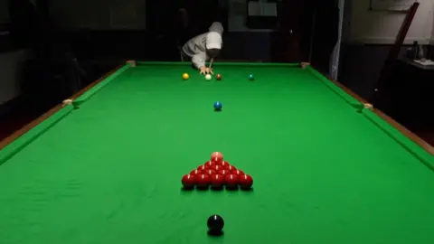 A man is about to strike some snooker balls with a cue