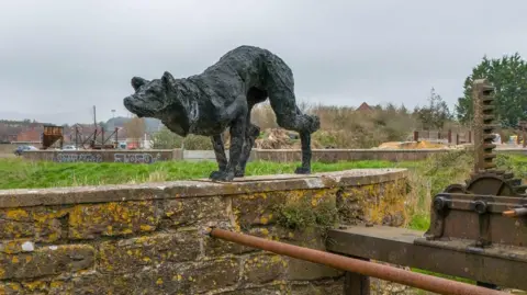 Neil Barnes The stalking dog sculpture on top of the wall above the weir at Bridport.