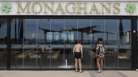 Two children, with their backs to the camera, look in the glass shuttered doors which seal off the outdoor seating area of Monagahans bar.