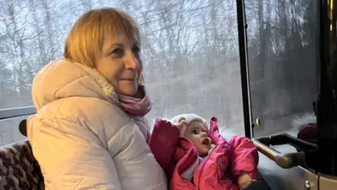 BBC A carer holds a child on a bus travelling to the Polish border