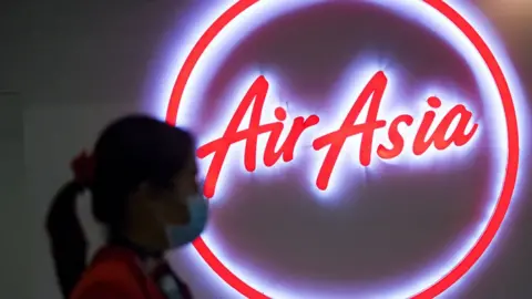 Getty Images Woman wearing a face mask walks past the logo of AirAsia at Don Mueang Airport in Bangkok, Thailand.