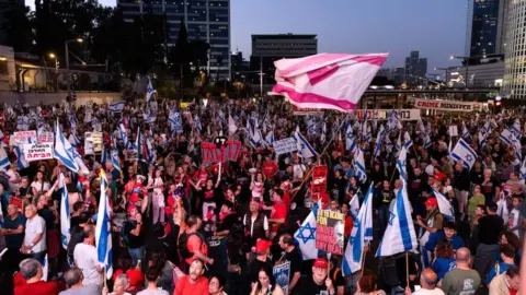 Amir Levy: Διαδηλωτές κρατούν σημαίες και πλακάτ κατά τη διάρκεια διαδήλωσης ζητώντας συμφωνία ομήρων