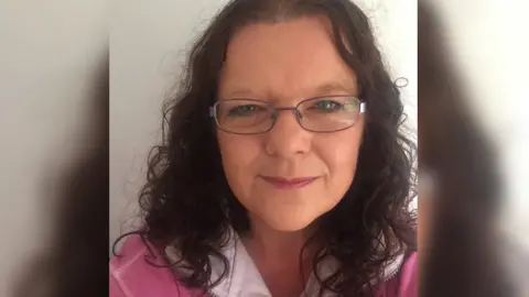 Julia Sealey Julia Sealey. She is wearing glasses and a pink and white shirt. She has dark curly hair. She is smiling at the camera.