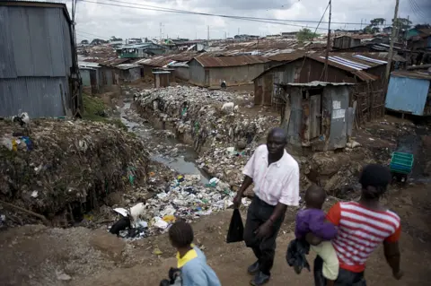 Getty Images Residents of Kibera walk past an open sewer