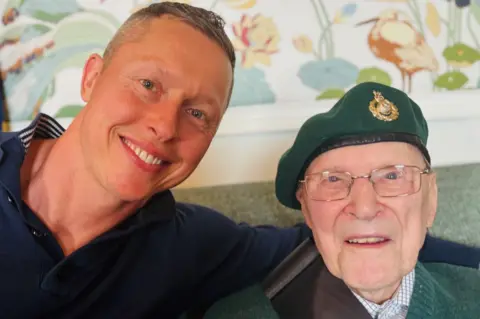 Army veteran Sandy Calder wearing a green beret and smiling and looking at the camera, next to his smiling grandson Cameron Calder.