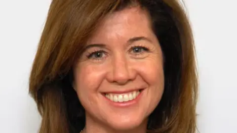 US Senate Elizabeth MacDonough has brown hair and is smiling in front of a white backdrop