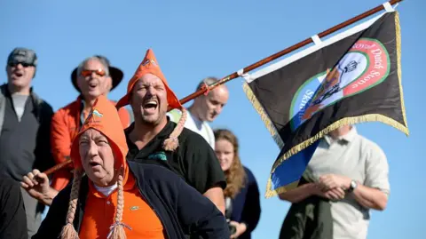 Getty Images Competitors and spectators wearing hats and carrying a flag at 2013's World Stone Skimming Championships