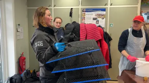 George Carden/BBC Lottie holding a plastic crate which has four layers where the oysters will live underwater