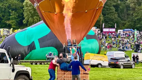 BBC Hot air balloons filling on the ground, one orange, another green and black