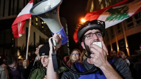 AFP A Lebanese protester speaks into a megaphone outside the home of Saad Hariri in Beirut (16 December 2019)