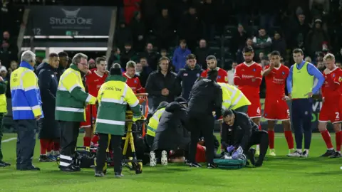 Wycombe players form a barrier around a fallen team-mate Tjay De Barr