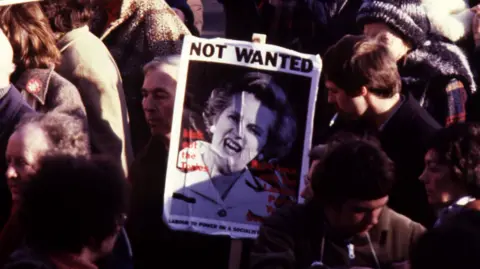 A crowd gather in Liverpool to protest about the unemployment rate during a Labour Party and Trade Unions rally in 1980. A placard has the words "Not Wanted" with a picture of Margaret Thatcher.