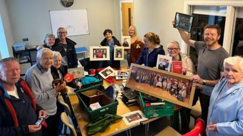 Greenisland Parish Church Parishioners are gathered round a table which has boxes of photographs on top of it celebrating the retrieval of the photos from the fire.