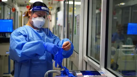 PA Media A member of staff puts on PPE at King's College Hospital in London