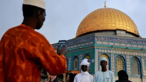 Reuters Two people posing while a third takes a picture of them in front of the golden dome of al-Aqsa mosque, Jerusalem.