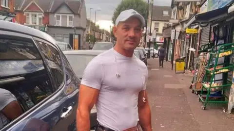 Met Police Image of Catalin Bostan, a man wearing a white baseball cap and tight white top, who is sought by police