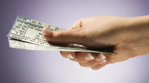 Rubberball/Mike Kemp A hand holding a pair of tickets