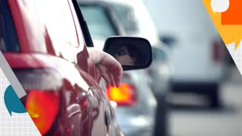 Alamy view of back of car, women's face in wing mirror as she looks at the queue of traffic ahead