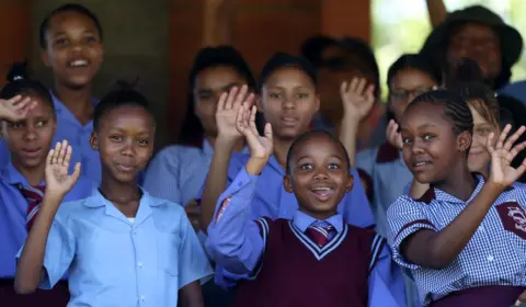 MATTHEW LEWIS/GETTY IMAGES Schoolchildren wave to the camera.