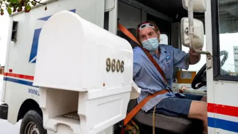 Getty Images A postal worker delivers mail wearing a mask