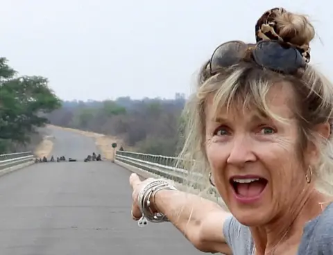 Maggie Crouch A woman points at a group of baboons on a road