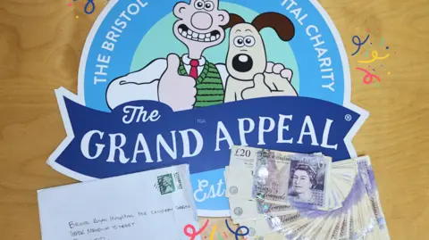 Grand Appeal An envelope and several £20 notes sit on top of the logo for Wallace and Gromit's Grand Appeal. The logo is blue and has drawing of Wallace and Gromit.